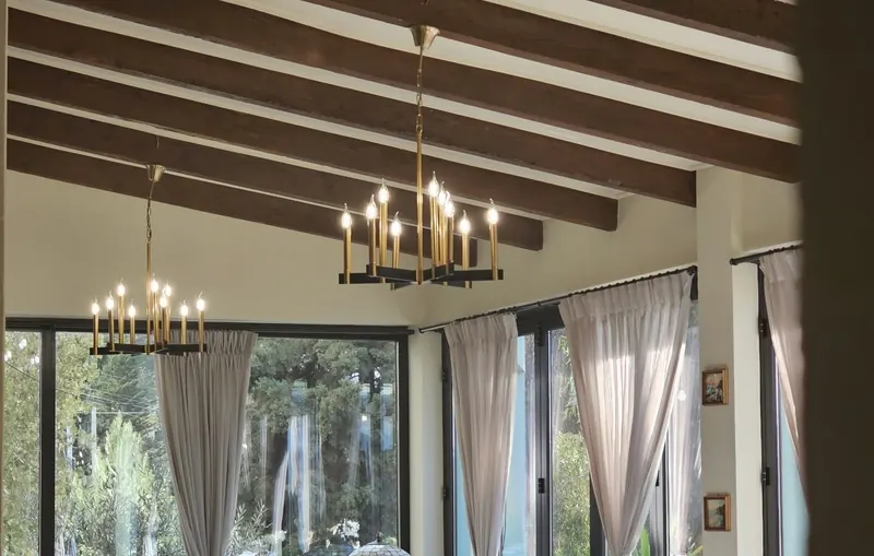 The main hall under wooden beams and chandeliers, with tall windows onto the garden