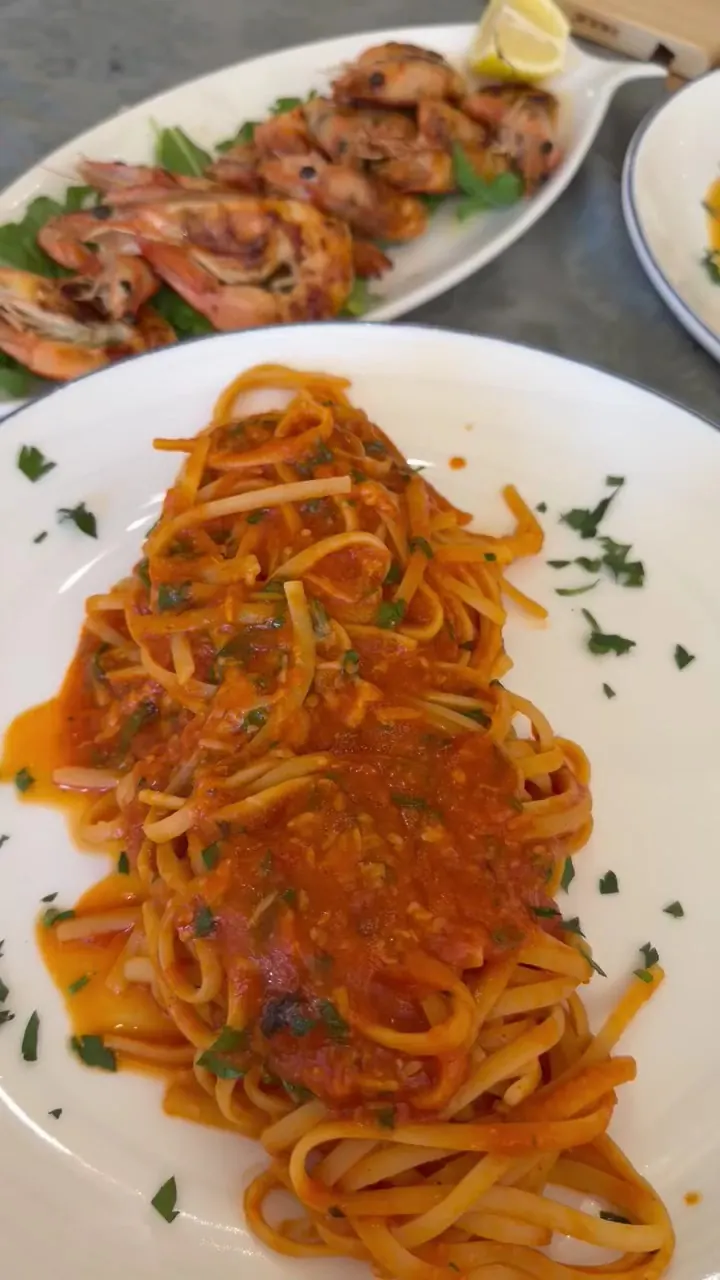 Linguine in a red seafood sauce, with grilled prawns behind