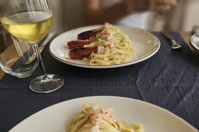 Tagliatelle with red prawns and a glass of white wine on a navy tablecloth