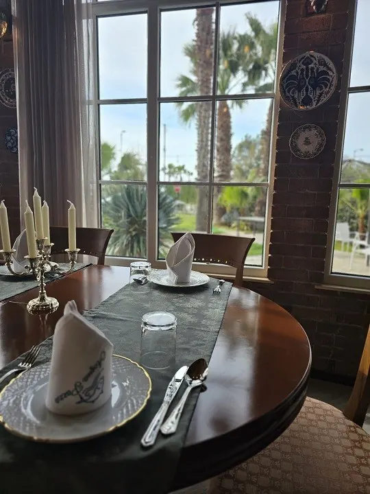 A table by the window with folded napkins, candles and palm trees outside